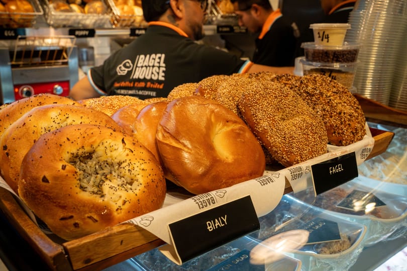 Freshly baked bagels and bialys displayed in a wooden basket at Bagel House, with staff in the background.